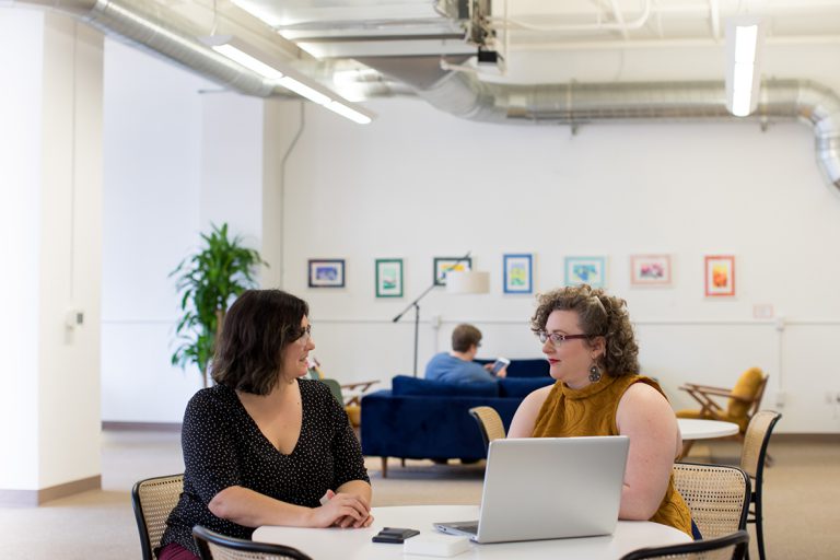 two women sitting at table with laptop